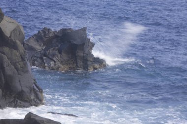Kayalık kıyı manzarası ve kayalara çarpan dalgalar.      