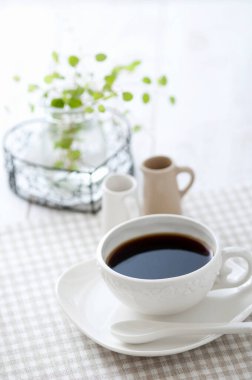 Beyaz bir masada bir fincan sade kahve ve kaşık..