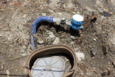 Açık hava borularını kuru toprak kalıntıları arasında birleştiren mavi su ölçer.