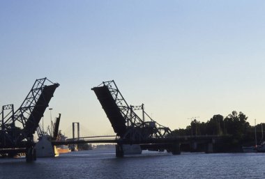 Gökyüzü açık iken sakin bir nehri kaplayan yükseltilmiş asma köprü