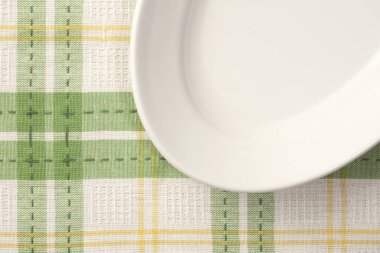 Arkaplanda kareli peçete olan beyaz tabak