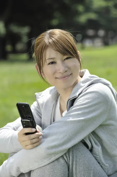 attractive young Asian woman with mobile phone in park.