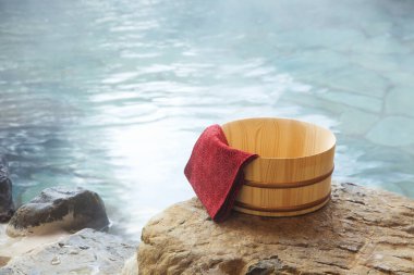 Japonya 'da açık hava banyosunda kayanın üzerinde kırmızı havlu ve bambu kovası.