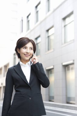 Şehirde cep telefonuyla konuşan gülümseyen genç bir kadının portresi.