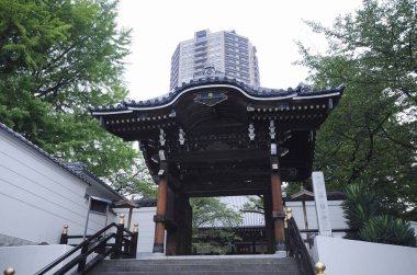 Geleneksel Japon kapısı modern binanın yanındaki yeşil ağaçların arasında duruyor.