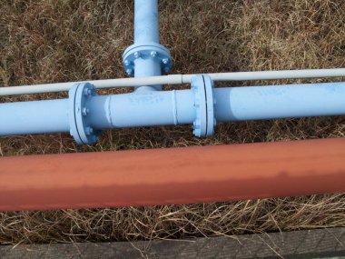 Mavi endüstriyel borular kuru kahverengi çimlerin üzerinde kesişiyor.