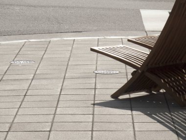 Gri fayanslı kaldırım köşesinde dinlenen tahta sandalye.