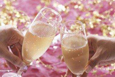 Arka planda şenlik dekoru olan şampanya kadehlerini tutan ellerin görüntüsünü kapat.