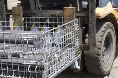 Endüstriyel forklift, ağır ekipmanlarla dolu metal kafes taşıyor.