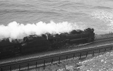 Eski trenin deniz kıyısı boyunca sürüşünün siyah beyaz fotoğrafı. 