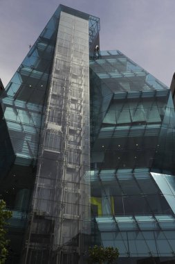 Gökyüzünü ve çevresindeki yeşilliği yansıtan modern cam bina