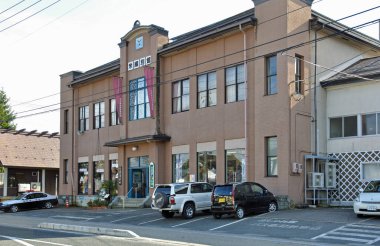 Geniş pencereli ve dışarıda park etmiş araçları olan modern bej bina.