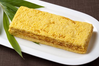 Beyaz tabakta yeşil yapraklı sarı Japon omleti.