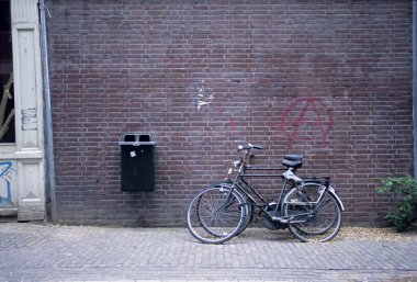 Binanın dışındaki çöp kutusunun yanındaki tuğladan duvara yaslanmış siyah bisiklet.