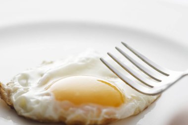 Kızarmış yumurta ve çatal beyaz tabakta. 