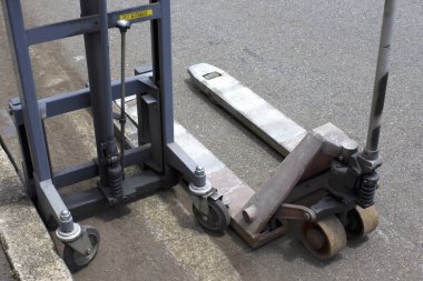 Metal forkliftin yanında duran endüstriyel palet krikosu açık havada beton kaldırımda.
