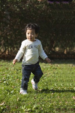 Parktaki çimlerde oynayan yakışıklı Asyalı çocuk. 