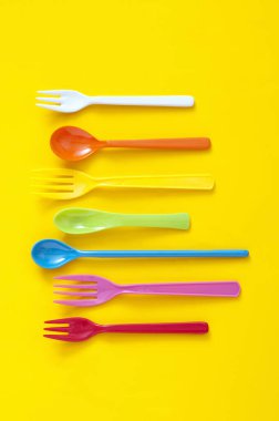 Sarı arka planda renkli plastik çatal bıçak seti. en üstteki görünüm     