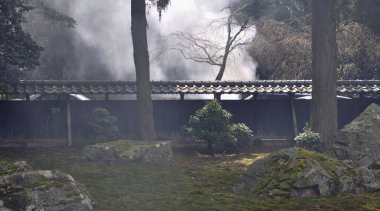 Geleneksel Japon bahçe duvarının yanındaki yüksek ağaçların arasından yükselen sis.