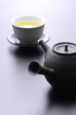 Beyaz arkaplanda bir fincan yeşil çay ve çaydanlık..