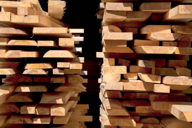 Yığılmış ahşap tahtalar kereste yığınları arasında dar bir geçit oluşturuyor.