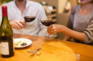 Asyalı bir adam ve kadın bir restoranda birlikte kırmızı şarap içiyorlar.