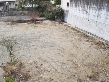 Beton duvarın ve seyrek bitki örtüsünün yanındaki boş çakıllar.