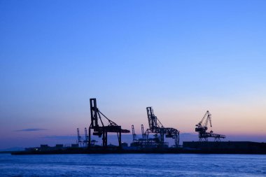 Gün batımında ve denizde siluet vinçler