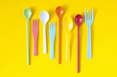 Sarı arka planda renkli plastik çatal bıçak seti. en üstteki görünüm     