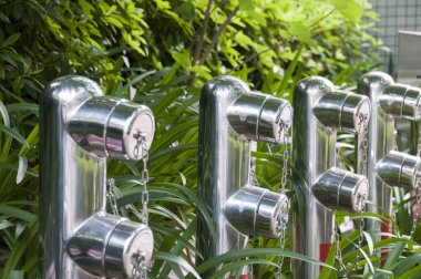 Açık havada yeşil yapraklı bitkilerin arasında duran parlak metal yangın muslukları.