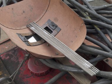 Karışık metal çubukların arasında duran eski kaynak miğferi.