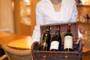 Hasır sepette üç şarap şişesi tutan kadın.