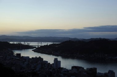 Akşamları nehir manzarası, karanlık tepeler ve binalar.