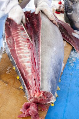 Ahşap tahtada büyük taze ton balığı kesen işçiler.