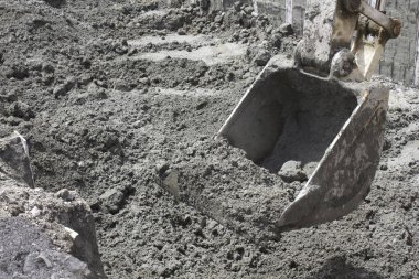 Kazı kovası gri inşaat sahası toprağını eşeliyor