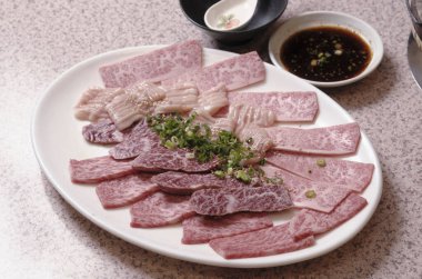 Beyaz tabakta düzgün sıralanmış çiğ et dilimleri.