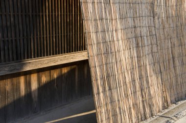 Güneş ışığı, dışarıda örülmüş bambu perdesine gölge düşürüyor.