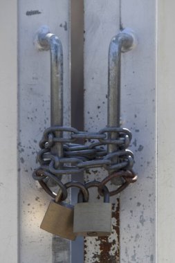 Paslı metal zincir iki asma kilit kullanarak çift kapı emniyete alıyor.