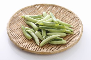 Beyaz arkaplanda bambu sepetinin üzerindeki taze bezelye kabuklarının yakın plan görüntüsü