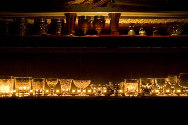 Parlak mumlar, koyu rafta duran zarif cam eşyalar.