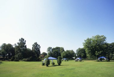 Berrak mavi gökyüzünün altında dağınık çadırların yer aldığı geniş çimenlik bir alan.