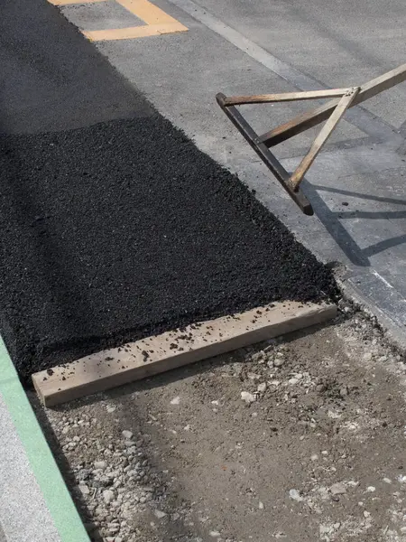 Yol yüzeyinde yeni yerleştirilmiş asfalt düzleştiriliyor.