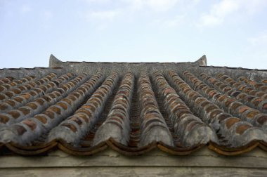 Yıpranmış kil çatı kiremitleri gökyüzüne karşı tekrarlanan desenler oluşturuyor
