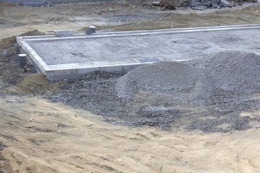 İnşaat alanındaki çakıl yığınlarıyla çevrili beton temeli