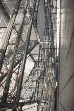 Şehir sokağı, binanın dış tarafındaki yoğun yapı iskelesi ve koruyucu ağ ile çerçevelenmiş ve kısmen gizlenmiş..