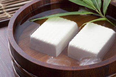Hiyayakko 'nun (soğuk tofu) ve yeşil bambu yapraklarının ahşap kovada su ile çekilmiş bir fotoğrafı.