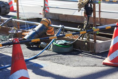 İnşaat alanı, kaldırımda turuncu koni ve ekipman gösteriyor.