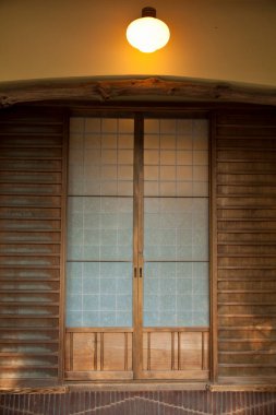 Ahşap kapı, yukarıdaki yuvarlak lambayla aydınlatılmış.