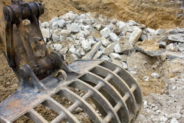 Paslı kazıcı pençesi dışarıda beton molozlarını tutuyor.