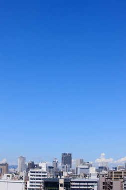 Açık mavi gökyüzü altında yüksek binaların yer aldığı modern şehir silüeti